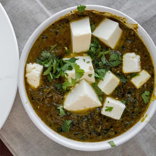 Overhead view of a white bowl filled with vibrant green Palak Paneer, garnished with fresh cilantro.