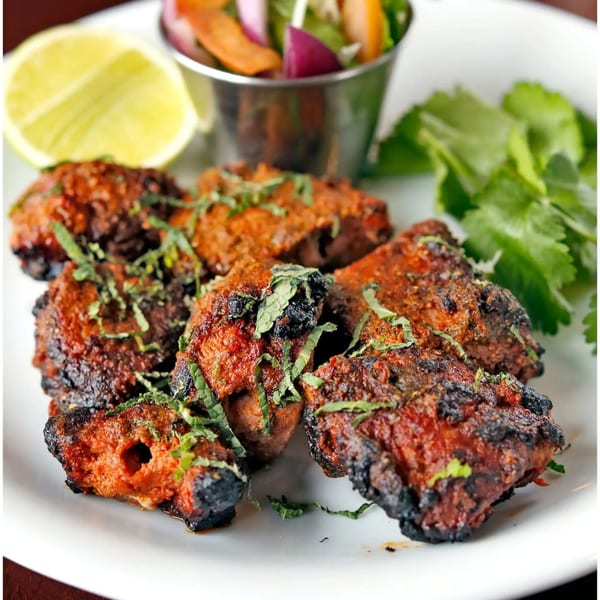 Mehfil Indian Cuisine's chicken tikka, garnished with mint, served with a lemon wedge and side salad.