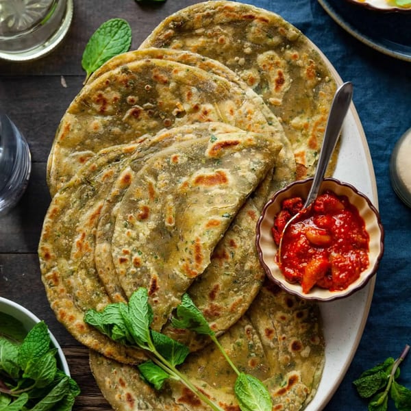 A plate of golden-brown Indian parathas with a side of vibrant red pickle and fresh mint.
