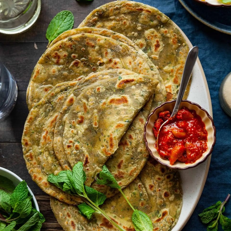A plate of golden-brown Indian parathas with a side of vibrant red pickle and fresh mint.