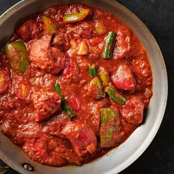 Close-up of a vibrant red Indian curry with chicken and green bell peppers in a metal pan.