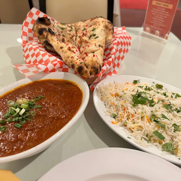 Indian meal with naan bread in a red and white checkered basket, a bowl of curry, and rice.